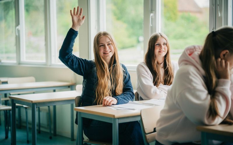 Elever i ett klassrum, en elev räcker upp handen